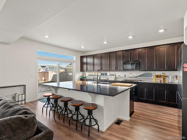 21901 E 42nd Pl, Aurora, CO 80019 - kitchen with black appliances, a kitchen breakfast bar, light wood finished floors, tasteful backsplash, and a center island with sink