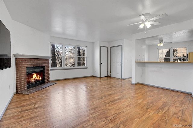 unfurnished living room with ceiling fan, a fireplace, and light hardwood / wood-style flooring