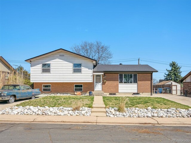 tri-level home with an outdoor structure, brick siding, and a front yard