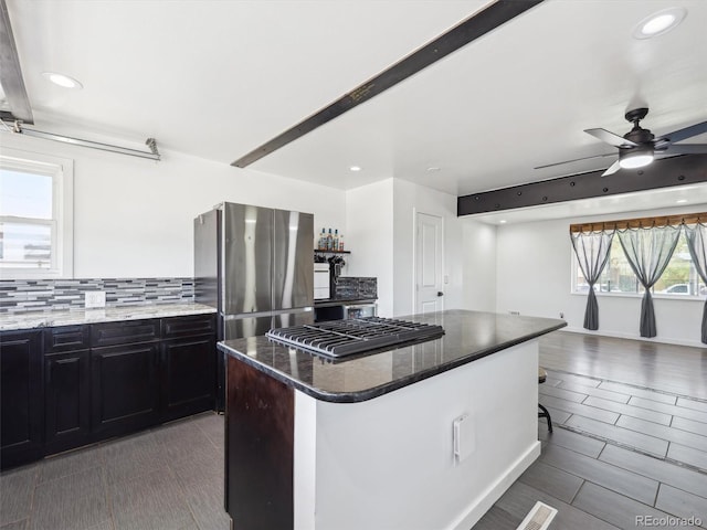 kitchen with a center island, tasteful backsplash, ceiling fan, dark cabinets, and appliances with stainless steel finishes