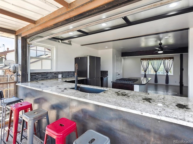 kitchen featuring a sink, ceiling fan, stone countertops, backsplash, and freestanding refrigerator