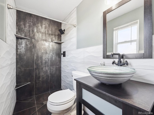 bathroom with tile walls, toilet, vanity, and tiled shower