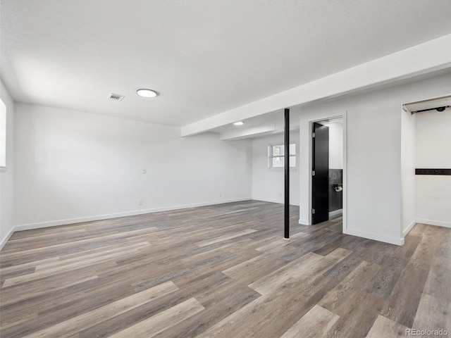 below grade area with wood finished floors, visible vents, and baseboards