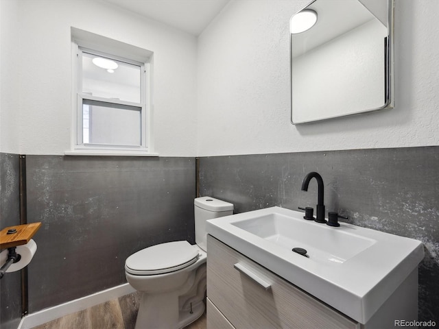 half bathroom featuring wood finished floors, vanity, and toilet