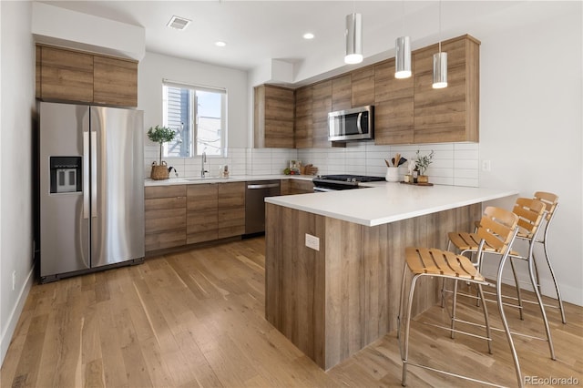 kitchen featuring appliances with stainless steel finishes, brown cabinetry, a sink, a peninsula, and recessed lighting