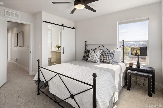 bedroom with light carpet, a barn door, a ceiling fan, baseboards, and ensuite bath