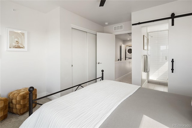 carpeted bedroom with a closet, connected bathroom, a barn door, baseboards, and ceiling fan