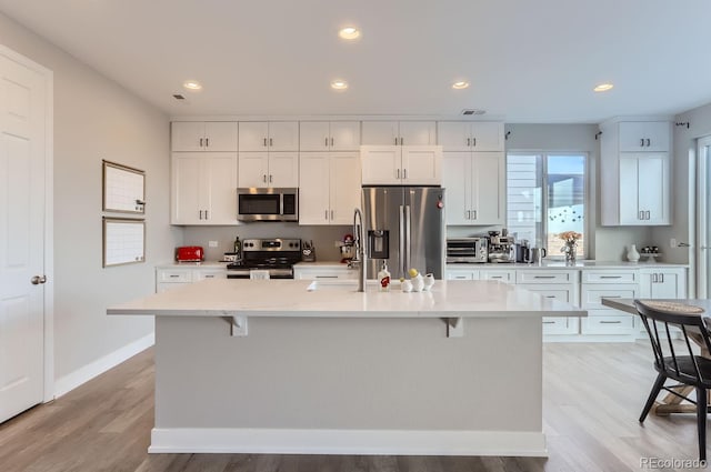 6645 Dry Fork Dr, Frederick, CO 80516 - kitchen featuring stainless steel appliances, light countertops, white cabinets, a kitchen bar, and an island with sink