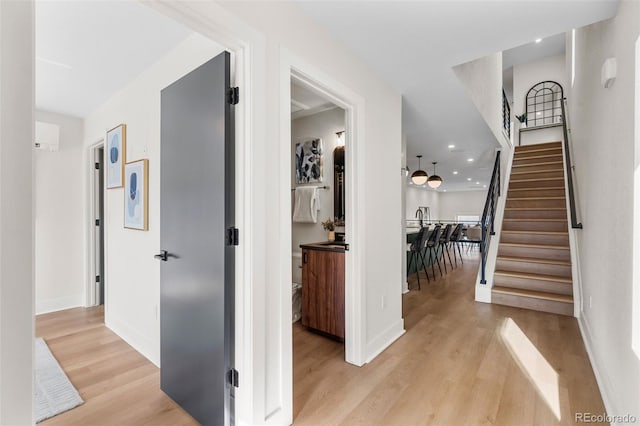 hallway with light wood finished floors, baseboards, stairs, and recessed lighting