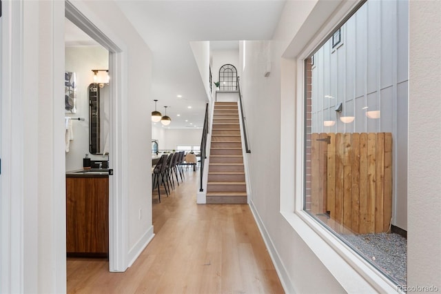 hall featuring light wood-style floors, stairs, and baseboards