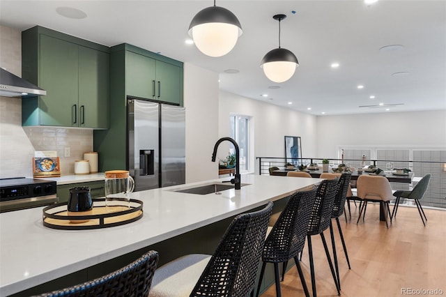 kitchen featuring stainless steel fridge with ice dispenser, green cabinetry, a sink, wall chimney exhaust hood, and light wood finished floors