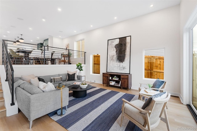 living area with light wood-style floors, recessed lighting, a towering ceiling, and stairway