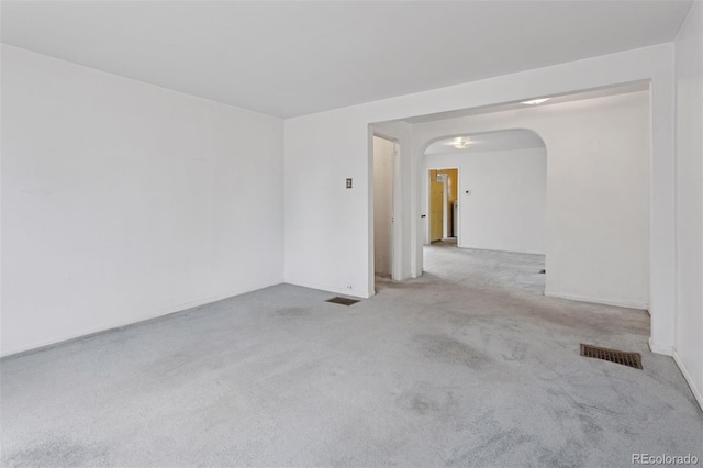 carpeted empty room featuring arched walkways, baseboards, and visible vents