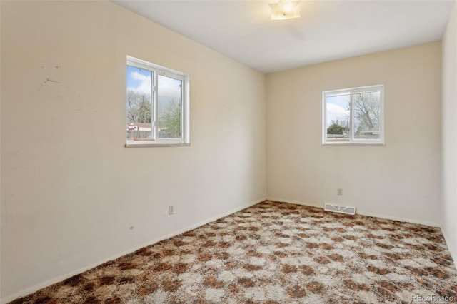 spare room featuring carpet floors, a wealth of natural light, baseboards, and visible vents