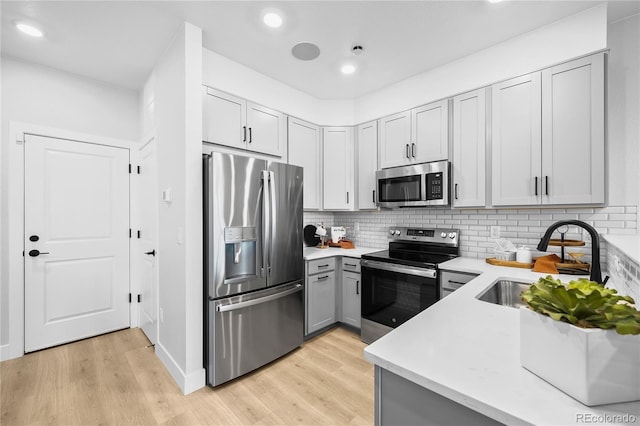17137 W 91st Ln, Arvada, CO 80007 - kitchen featuring stainless steel appliances, gray cabinets, light countertops, tasteful backsplash, and light wood-style flooring