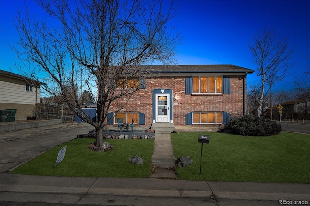 raised ranch with driveway, fence, a front lawn, and brick siding