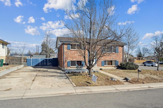 view of front facade featuring driveway, fence, and brick siding