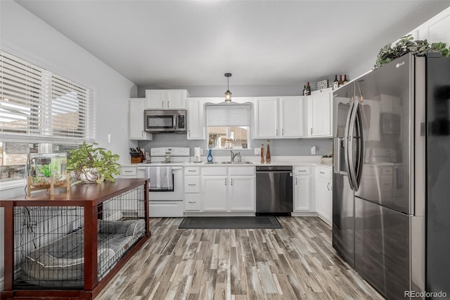 kitchen with wood-type flooring, sink, hanging light fixtures, stainless steel appliances, and white cabinets