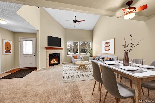 dining space featuring light carpet, ceiling fan, high vaulted ceiling, a tile fireplace, and baseboards