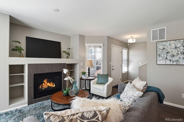 living room with visible vents, a fireplace, baseboards, and wood finished floors