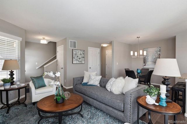 living area featuring baseboards, visible vents, stairway, wood finished floors, and an inviting chandelier