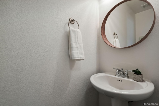 bathroom with a textured wall, visible vents, and a sink