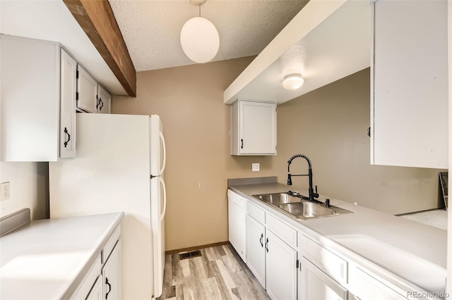 kitchen with a sink, white appliances, light wood finished floors, white cabinetry, and a textured ceiling