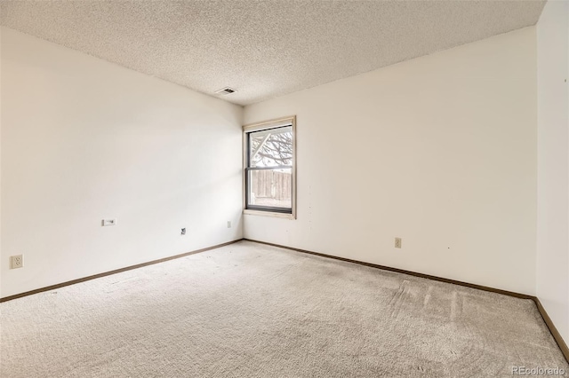 spare room featuring light colored carpet, baseboards, and a textured ceiling