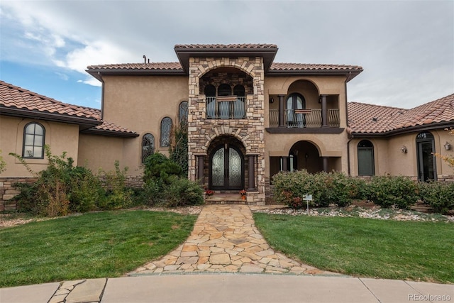 mediterranean / spanish house with a front yard, french doors, a balcony, and stucco siding