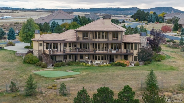 rear view of house featuring a patio, a balcony, a tile roof, stucco siding, and a chimney