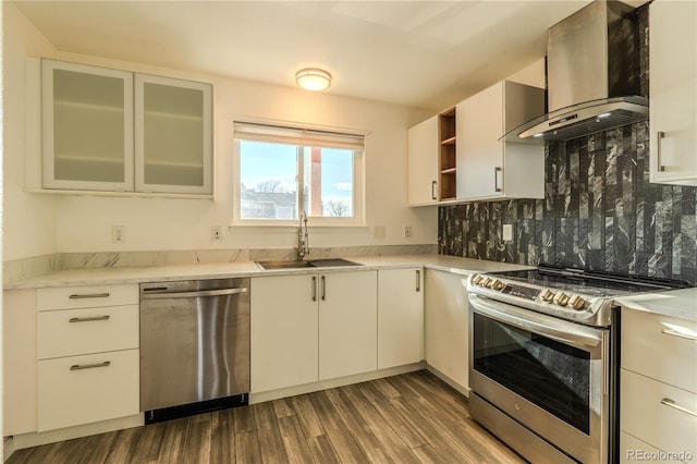 kitchen with appliances with stainless steel finishes, wall chimney exhaust hood, dark wood-type flooring, sink, and white cabinetry