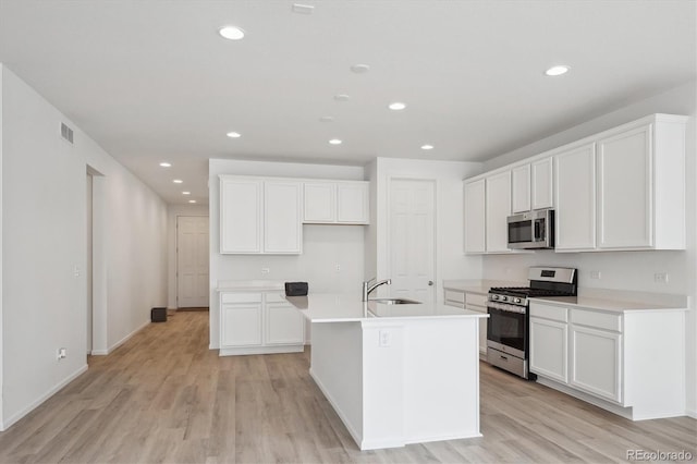 kitchen featuring white cabinetry, sink, stainless steel appliances, a kitchen island with sink, and light wood-type flooring