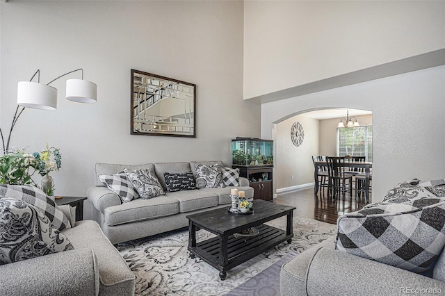 living room with arched walkways, a chandelier, wood finished floors, baseboards, and a high ceiling