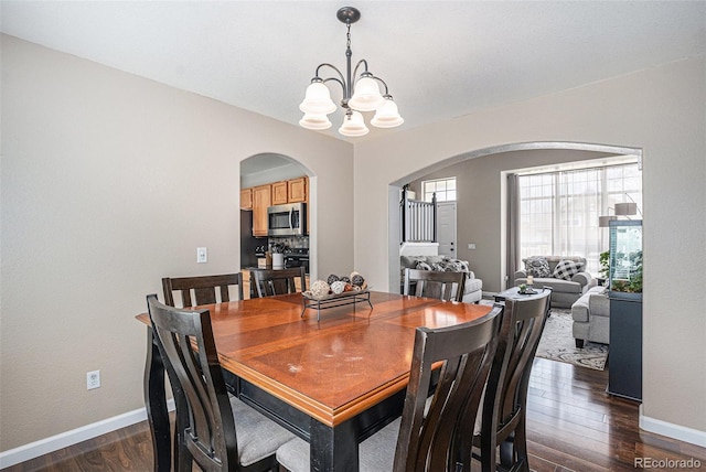 dining space with arched walkways, a chandelier, dark wood-style floors, and baseboards