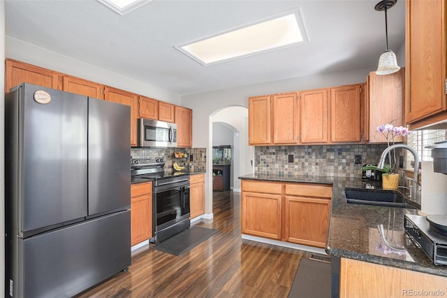 kitchen featuring stainless steel appliances, a sink, arched walkways, dark wood-style flooring, and decorative backsplash