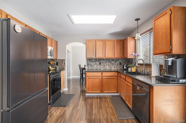 kitchen featuring appliances with stainless steel finishes, a sink, dark wood-type flooring, backsplash, and arched walkways