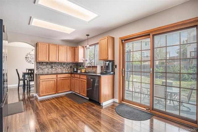kitchen featuring dishwashing machine, a sink, dark wood-style floors, dark countertops, and decorative backsplash