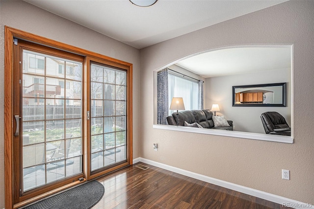 doorway featuring arched walkways, baseboards, and dark wood-style floors