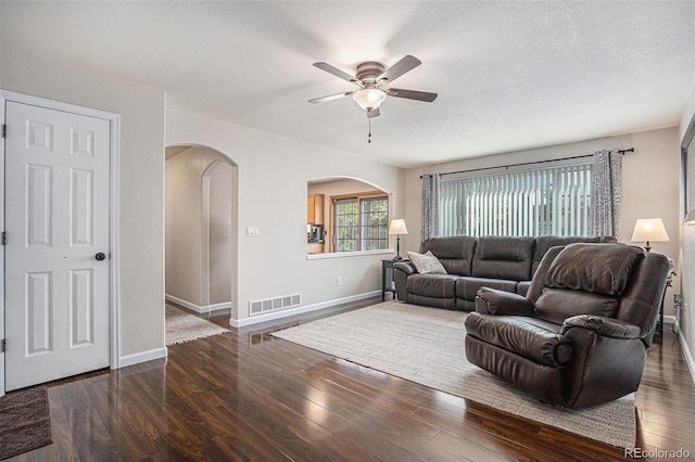 living area with arched walkways, wood finished floors, ceiling fan, baseboards, and a textured ceiling