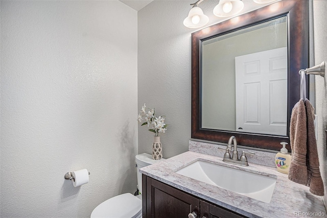bathroom featuring toilet, a textured wall, and vanity