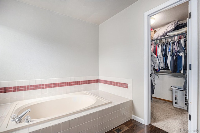 full bath with a spacious closet, a garden tub, baseboards, and wood finished floors