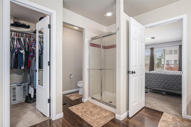 ensuite bathroom with wood finished floors, toilet, a shower stall, a spacious closet, and baseboards