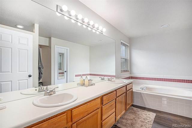 bathroom featuring a bath, wood finished floors, double vanity, and a textured ceiling
