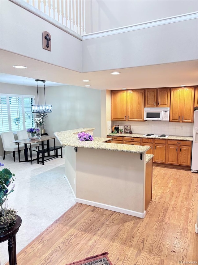 kitchen featuring pendant lighting, white appliances, light hardwood / wood-style flooring, and tasteful backsplash