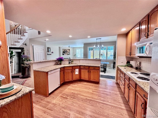 kitchen with light stone countertops, white appliances, decorative light fixtures, and light hardwood / wood-style floors