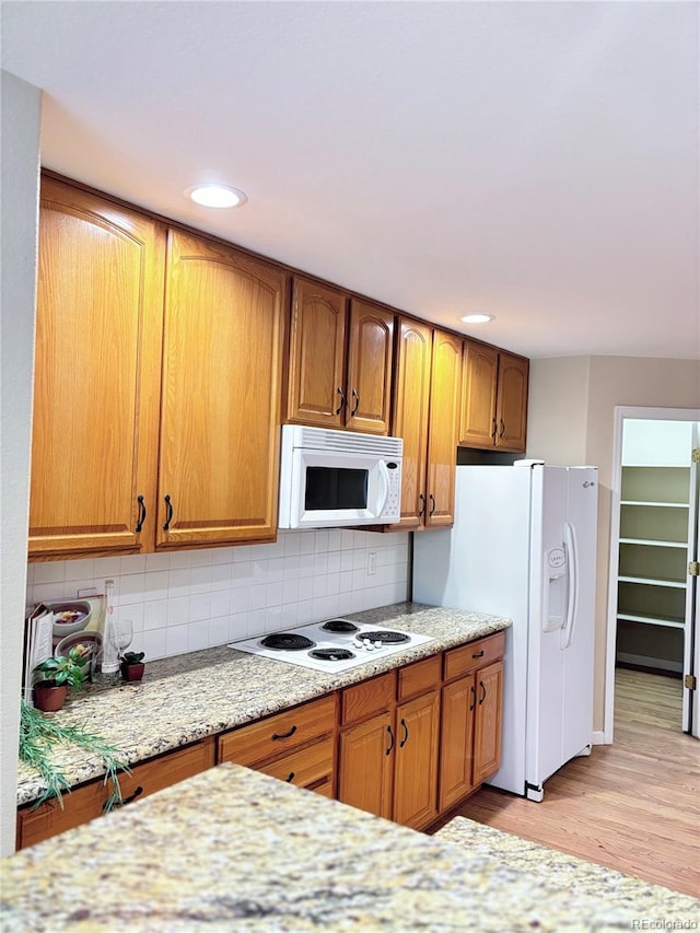 kitchen with light stone counters, white appliances, decorative backsplash, and light wood-type flooring