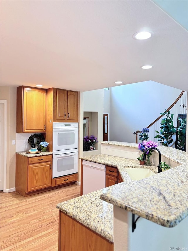 kitchen with sink, light stone counters, kitchen peninsula, white appliances, and light hardwood / wood-style floors