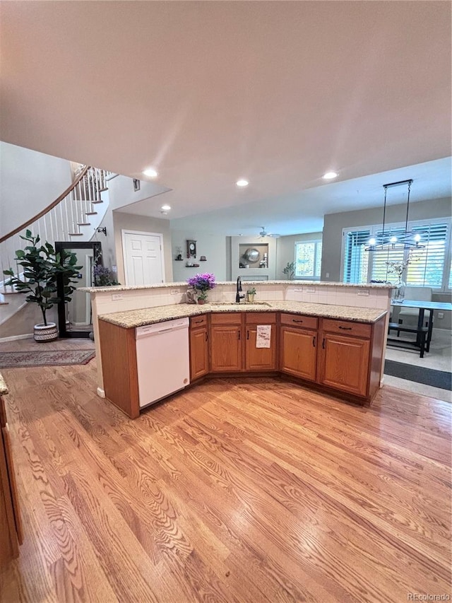 kitchen with decorative light fixtures, dishwasher, sink, light hardwood / wood-style floors, and a center island with sink