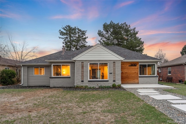view of front of home featuring a shingled roof and a yard