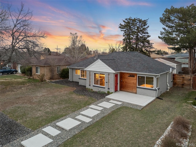 view of front facade with a front yard, fence, and roof with shingles